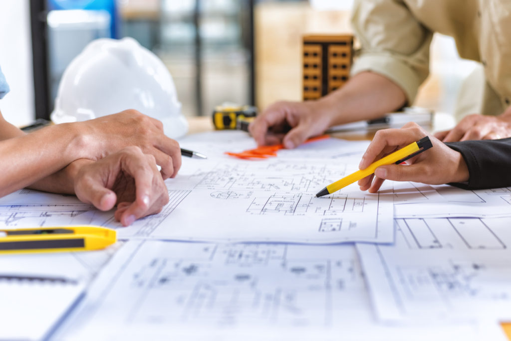 A team of engineers checking on construction blueprints on new project with engineering tools at an office desk.