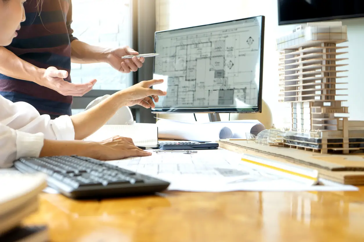 Architects in an office looking at a computer while discussing a digital drawing of their building plan.