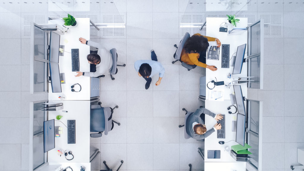 Facilities managers operational improvement - a male FM walking between rows of employees in an optimized workplace.